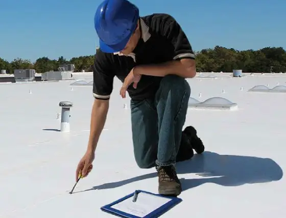 Commercial roofing inspector evaluating flat membrane roof surface for damage and performance in Central Illinois